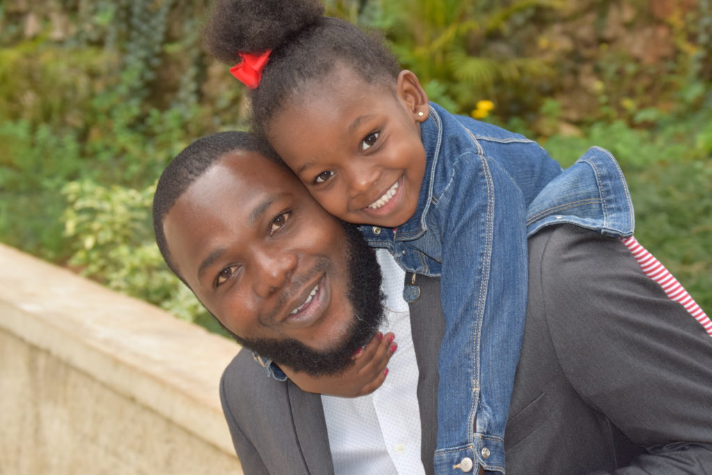 Medewerker van ons kinderdorp in Haïti en klein meisje op zijn rug.